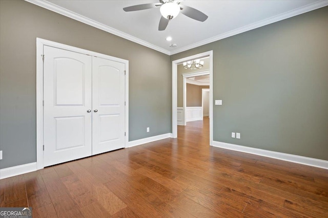 unfurnished bedroom with hardwood / wood-style floors, crown molding, ceiling fan with notable chandelier, and a closet