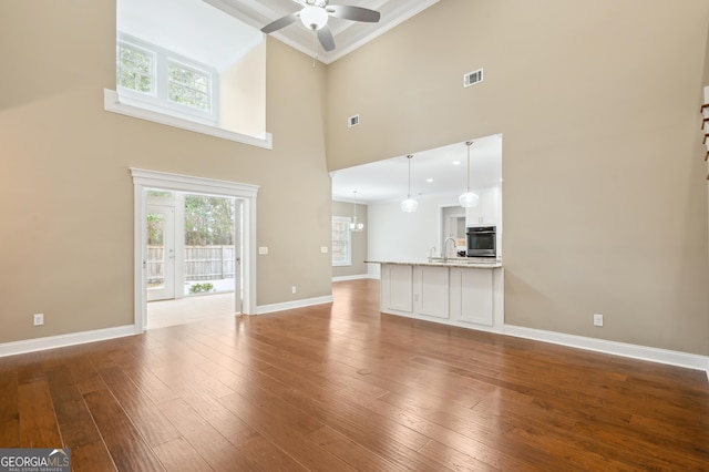 unfurnished living room featuring hardwood / wood-style floors, a towering ceiling, ornamental molding, and ceiling fan