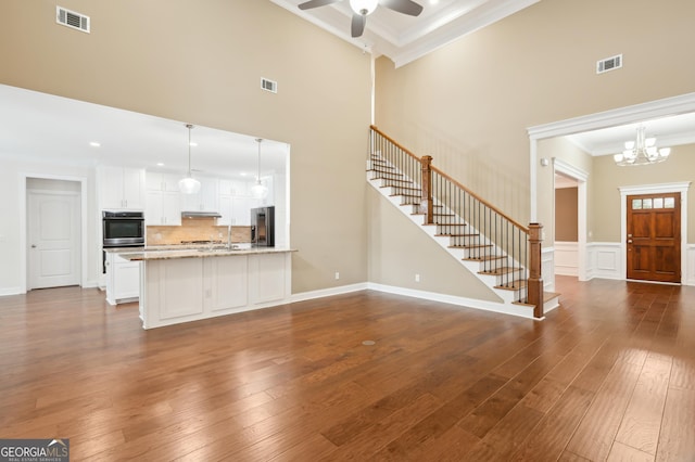 unfurnished living room featuring crown molding, dark wood-type flooring, ceiling fan with notable chandelier, and a high ceiling