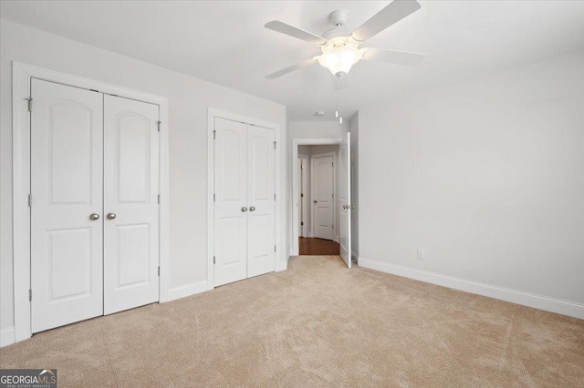 unfurnished bedroom with light carpet, two closets, and ceiling fan