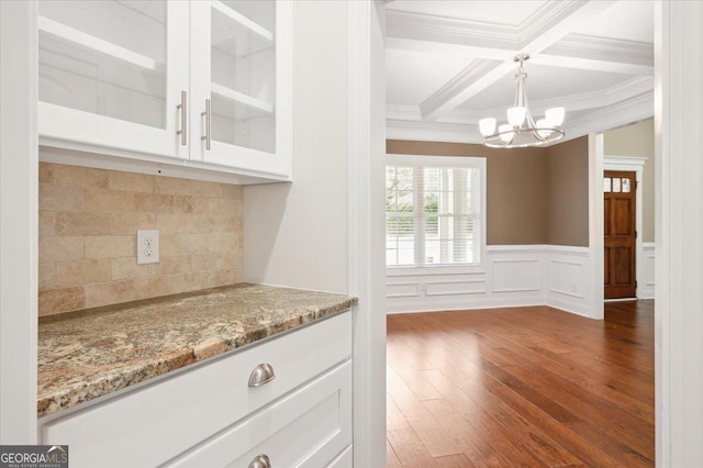 kitchen with dark wood-type flooring, coffered ceiling, light stone counters, hanging light fixtures, and white cabinets