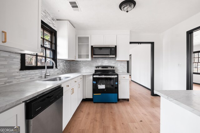 kitchen with appliances with stainless steel finishes, sink, white cabinets, backsplash, and light hardwood / wood-style flooring