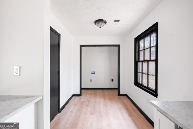 corridor featuring light hardwood / wood-style flooring, a textured ceiling, and a wealth of natural light