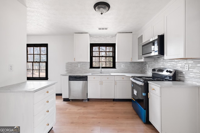 kitchen featuring tasteful backsplash, white cabinetry, sink, light hardwood / wood-style floors, and stainless steel appliances