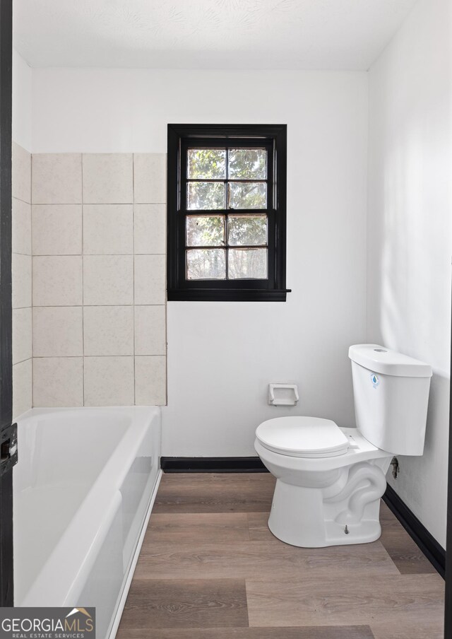 bathroom with a bathtub, hardwood / wood-style flooring, and toilet