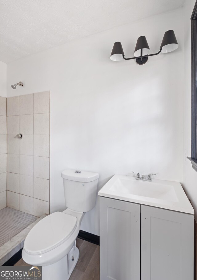 bathroom featuring tiled shower, wood-type flooring, toilet, and vanity