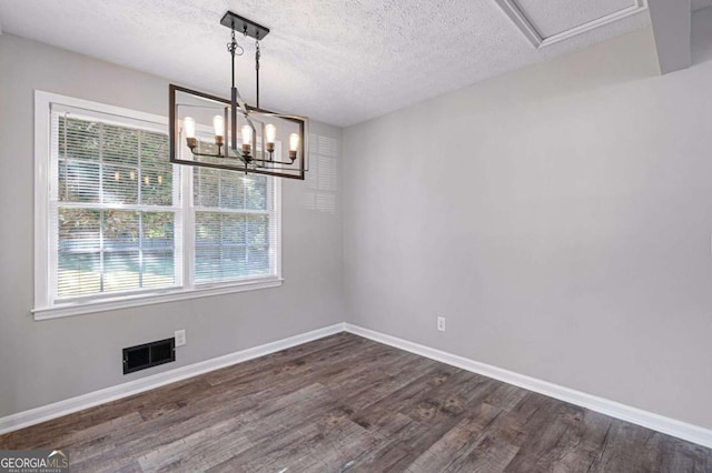 unfurnished dining area with dark wood-type flooring, a notable chandelier, and a textured ceiling