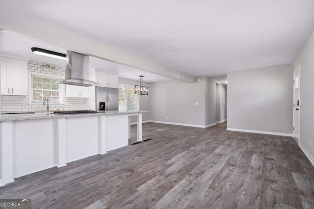 kitchen featuring white cabinetry, ventilation hood, hanging light fixtures, stainless steel fridge, and decorative backsplash