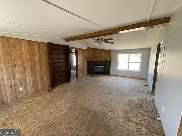 unfurnished living room with ceiling fan, carpet, a fireplace, lofted ceiling with beams, and wood walls