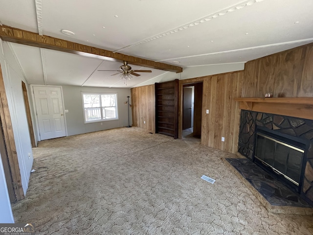 unfurnished living room with a stone fireplace, wooden walls, lofted ceiling with beams, carpet floors, and ceiling fan