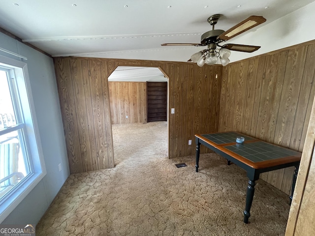 unfurnished dining area featuring ceiling fan, vaulted ceiling, carpet, and wood walls