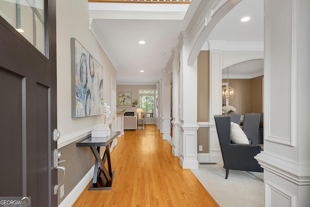 foyer entrance featuring crown molding, an inviting chandelier, decorative columns, and light wood-type flooring