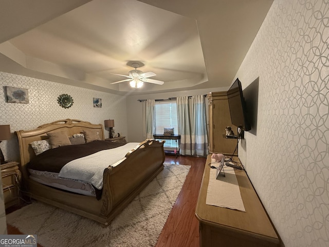 bedroom with a tray ceiling, dark hardwood / wood-style floors, and ceiling fan