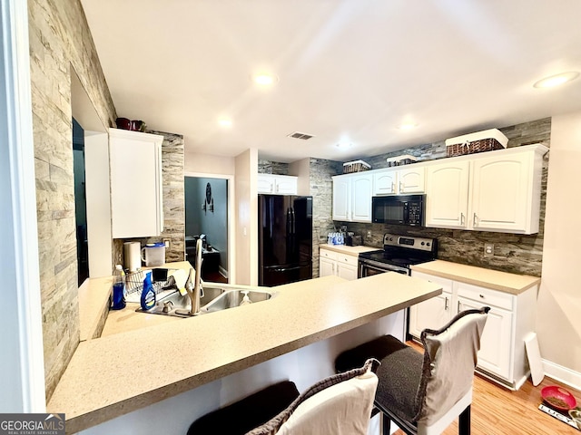 kitchen with visible vents, a peninsula, a kitchen breakfast bar, black appliances, and a sink