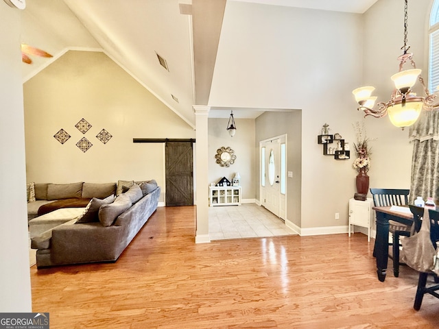 entryway with a notable chandelier, high vaulted ceiling, wood finished floors, a barn door, and baseboards