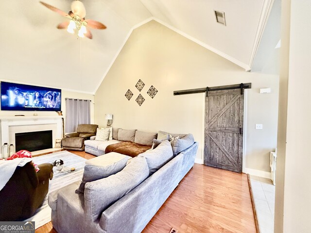 living area featuring ceiling fan, a barn door, ornamental molding, wood finished floors, and high vaulted ceiling