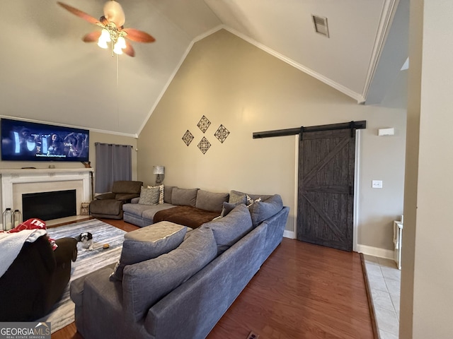 living room featuring wood-type flooring, high vaulted ceiling, ornamental molding, ceiling fan, and a barn door