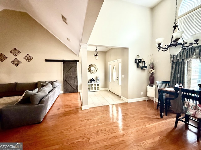 foyer with a notable chandelier, high vaulted ceiling, a barn door, and wood finished floors