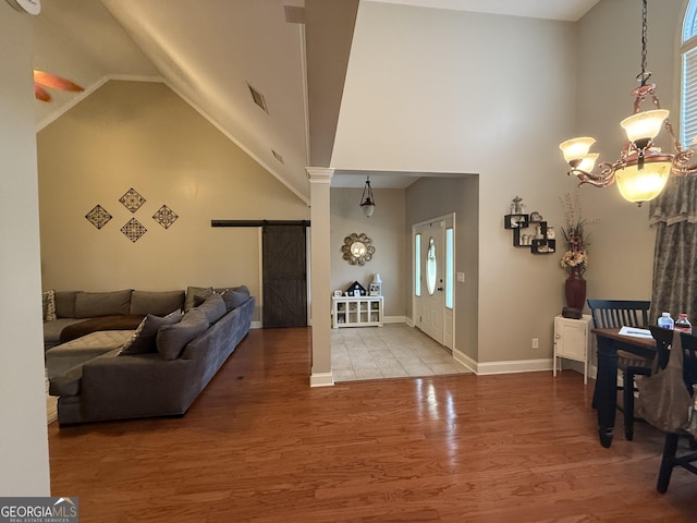 interior space featuring hardwood / wood-style floors, a notable chandelier, high vaulted ceiling, and a barn door