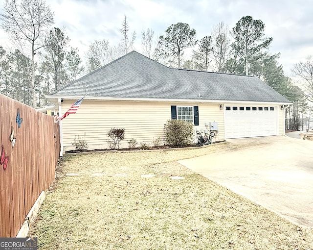 exterior space with a shingled roof, an attached garage, concrete driveway, and fence