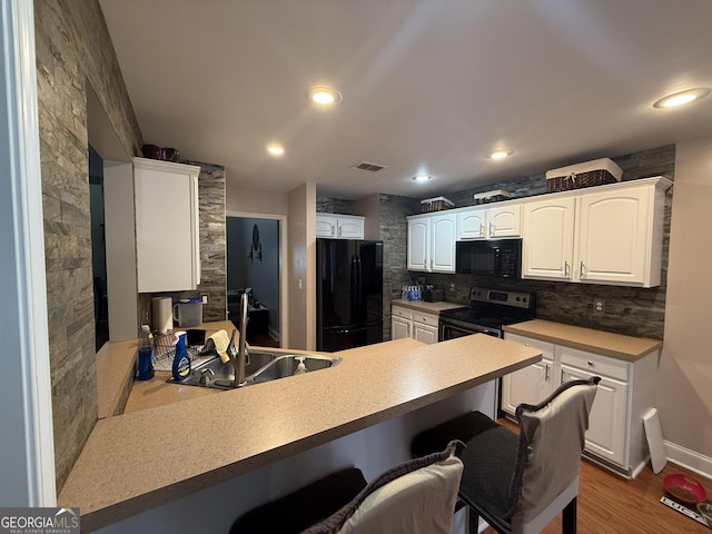 kitchen featuring black appliances, sink, white cabinets, a kitchen bar, and kitchen peninsula