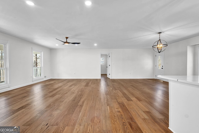 unfurnished living room with ceiling fan with notable chandelier and light hardwood / wood-style flooring