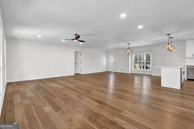 unfurnished living room with ceiling fan with notable chandelier and light hardwood / wood-style floors