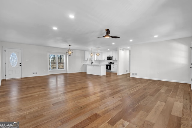 unfurnished living room with sink, ceiling fan with notable chandelier, and light wood-type flooring