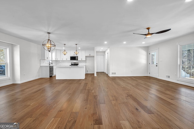 unfurnished living room featuring wood-type flooring and ceiling fan with notable chandelier