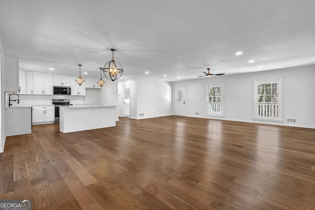 unfurnished living room featuring hardwood / wood-style flooring, sink, and ceiling fan with notable chandelier