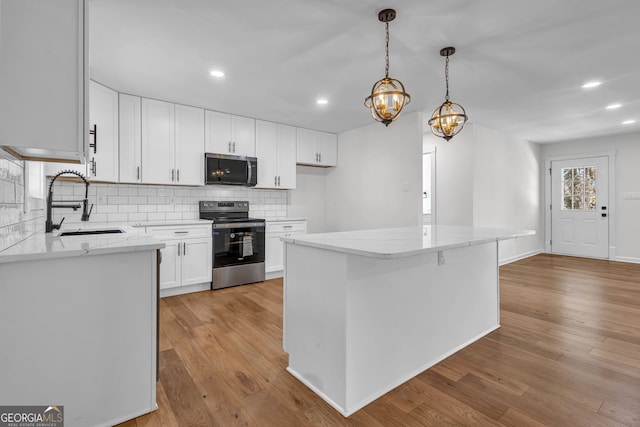 kitchen featuring pendant lighting, sink, stainless steel appliances, light hardwood / wood-style floors, and white cabinets