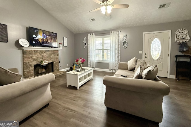 living room featuring lofted ceiling, dark wood-type flooring, a stone fireplace, and a textured ceiling