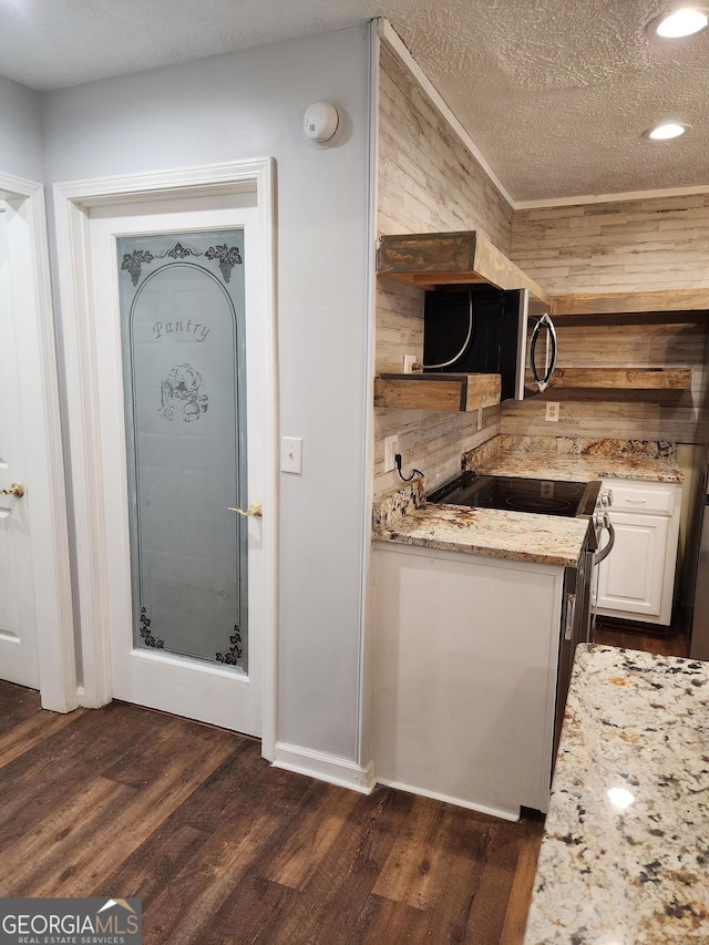 kitchen with white cabinetry, stainless steel range with electric stovetop, a textured ceiling, dark hardwood / wood-style flooring, and light stone countertops