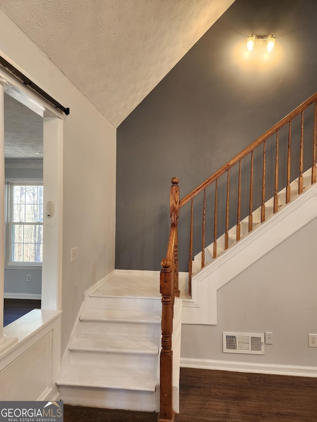 staircase featuring lofted ceiling, hardwood / wood-style flooring, a barn door, and a textured ceiling