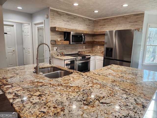 kitchen featuring appliances with stainless steel finishes, white cabinetry, sink, light stone countertops, and a textured ceiling