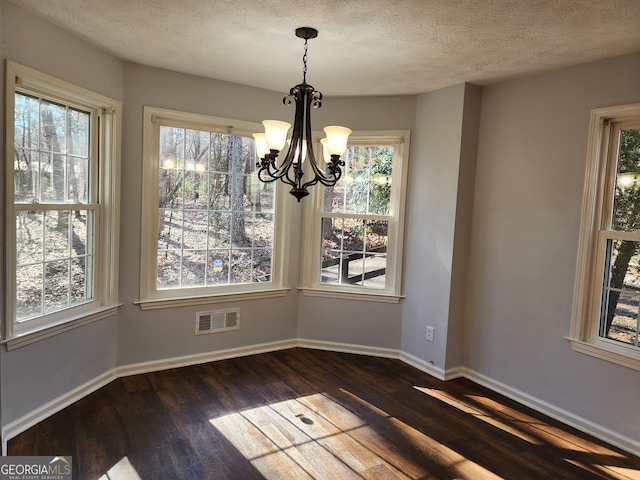 unfurnished dining area with a textured ceiling, a notable chandelier, and dark hardwood / wood-style flooring