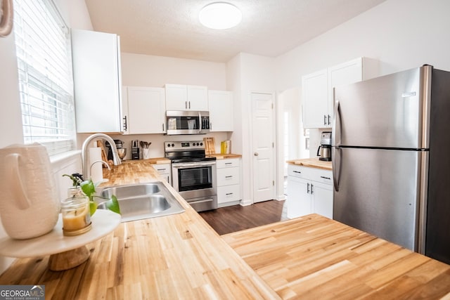 kitchen featuring wood counters, sink, a textured ceiling, stainless steel appliances, and white cabinets