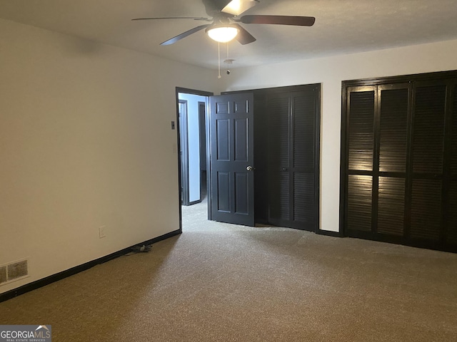 unfurnished bedroom with carpet flooring, two closets, and ceiling fan