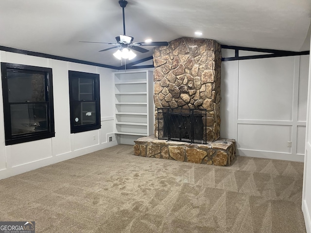 unfurnished living room with a stone fireplace, lofted ceiling, carpet floors, ceiling fan, and built in shelves