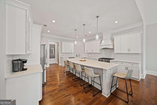 kitchen featuring stainless steel refrigerator, white cabinetry, a breakfast bar area, range, and custom range hood