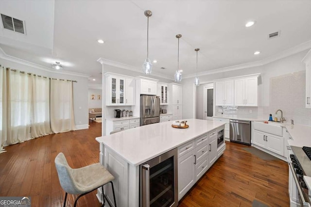 kitchen featuring decorative light fixtures, a center island, appliances with stainless steel finishes, beverage cooler, and white cabinets