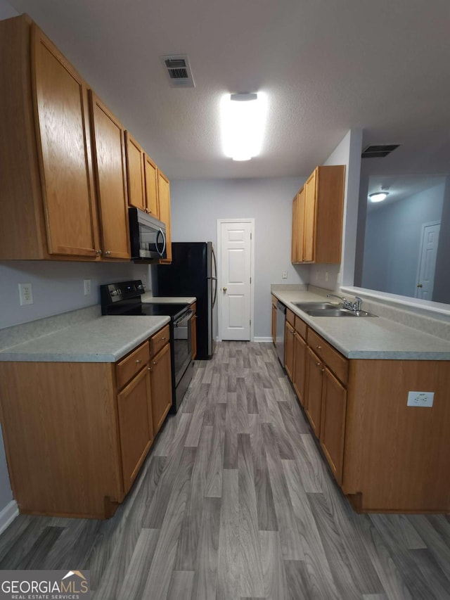 kitchen with light hardwood / wood-style floors, appliances with stainless steel finishes, kitchen peninsula, and sink