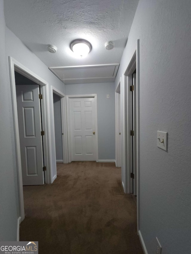 hallway with a textured ceiling and dark colored carpet