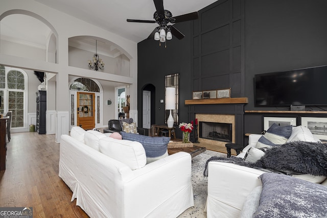 living room with a high ceiling, ceiling fan with notable chandelier, hardwood / wood-style floors, and a fireplace