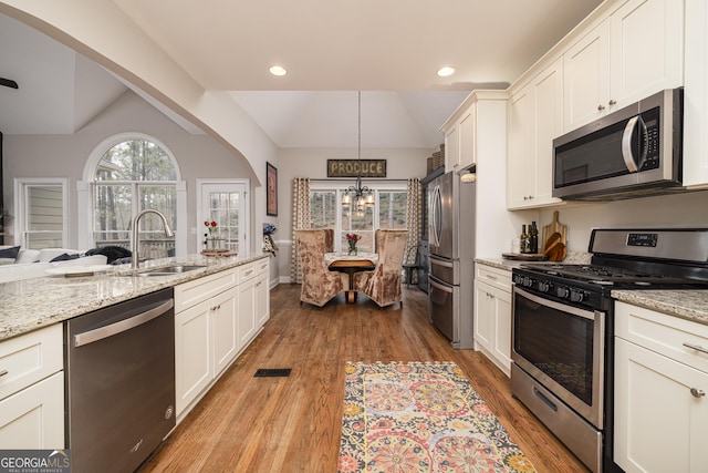 kitchen with sink, decorative light fixtures, vaulted ceiling, appliances with stainless steel finishes, and light stone countertops