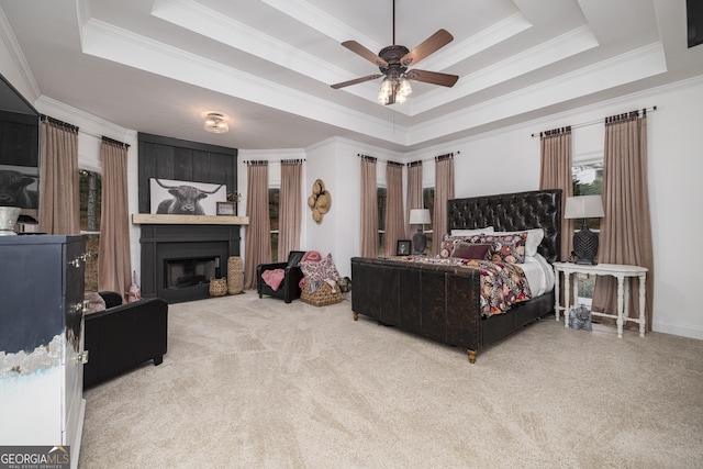 carpeted bedroom with ceiling fan, a large fireplace, ornamental molding, and a tray ceiling