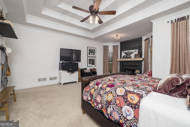 carpeted bedroom with ornamental molding, ceiling fan, a fireplace, and a tray ceiling