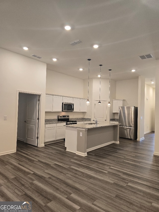 kitchen with pendant lighting, appliances with stainless steel finishes, white cabinetry, light stone counters, and a center island with sink