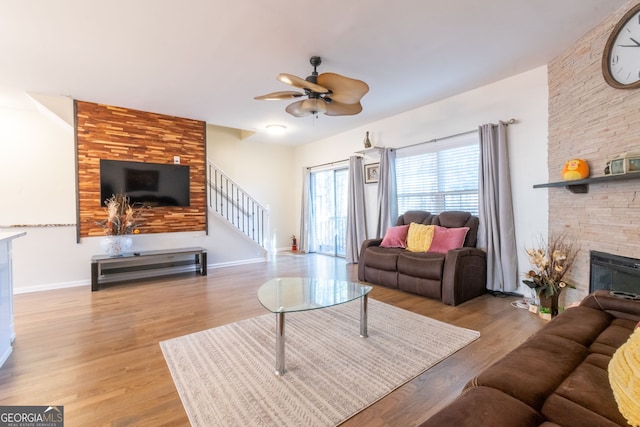 living area featuring a ceiling fan, wood finished floors, stairway, a large fireplace, and baseboards