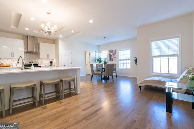 kitchen featuring hanging light fixtures, tasteful backsplash, white cabinets, stainless steel electric range oven, and wall chimney exhaust hood